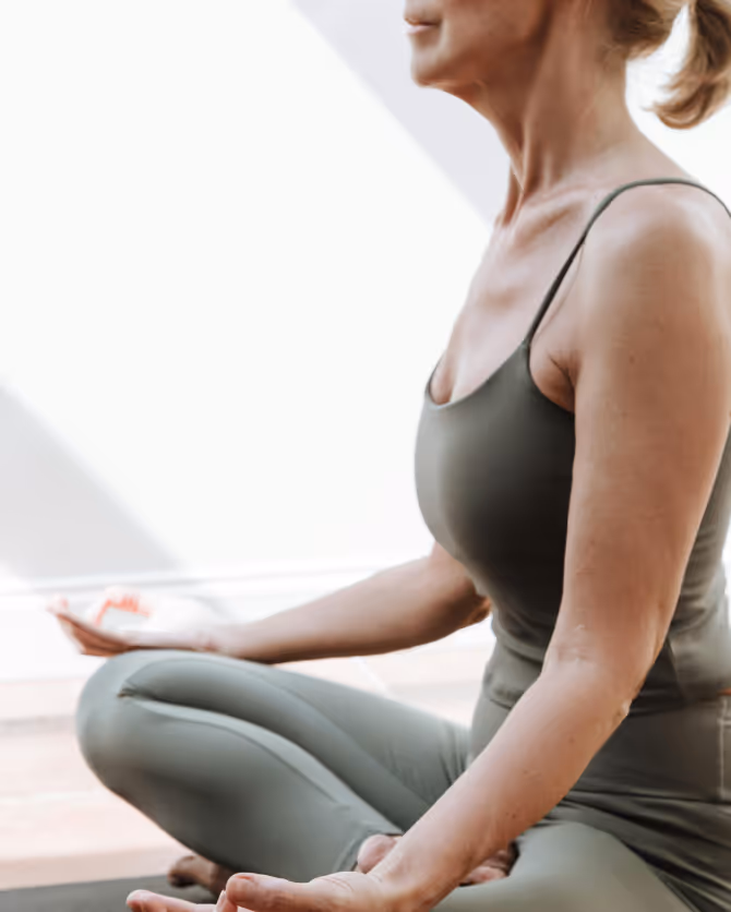 Woman sitting cross-legged in meditation, hands resting on her knees, in a sunlit room