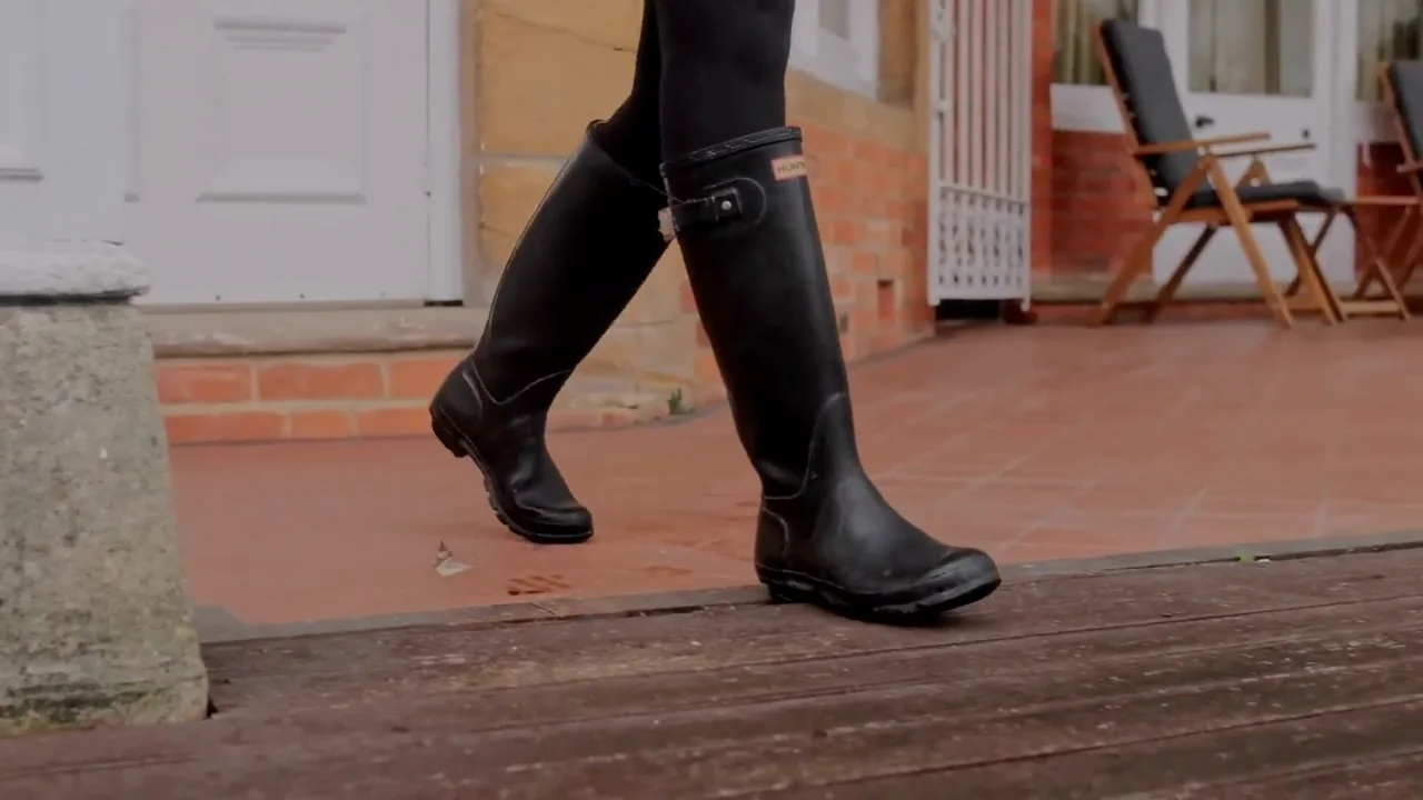 A woman walking across the tiled porch at River Arts Club in tall black wellington boots